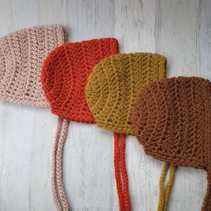 May include: Four crocheted baby bonnets in pink, red, mustard yellow, and brown.