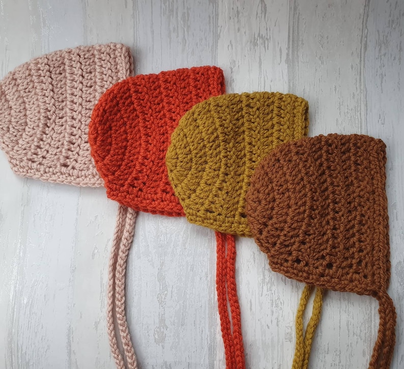 May include: Four crocheted baby bonnets in pink, red, mustard yellow, and brown.