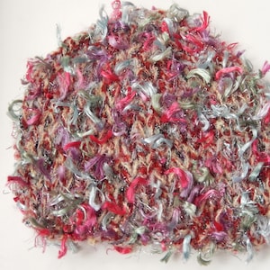 Puede incluir: Un gorro de punto rojo, rosa y azul con una textura esponjosa. El gorro está hecho con una variedad de hilos, incluyendo algunos con un brillo metálico.