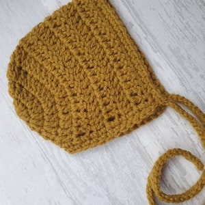 May include: A mustard yellow crocheted baby bonnet with ties.
