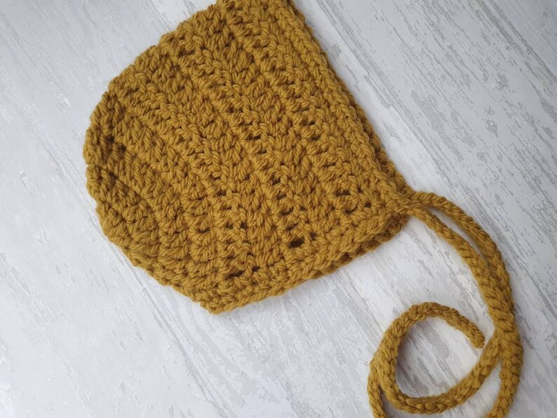 May include: A mustard yellow crocheted baby bonnet with ties.