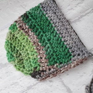 May include: A crocheted baby hat with stripes of green, brown and grey yarn.