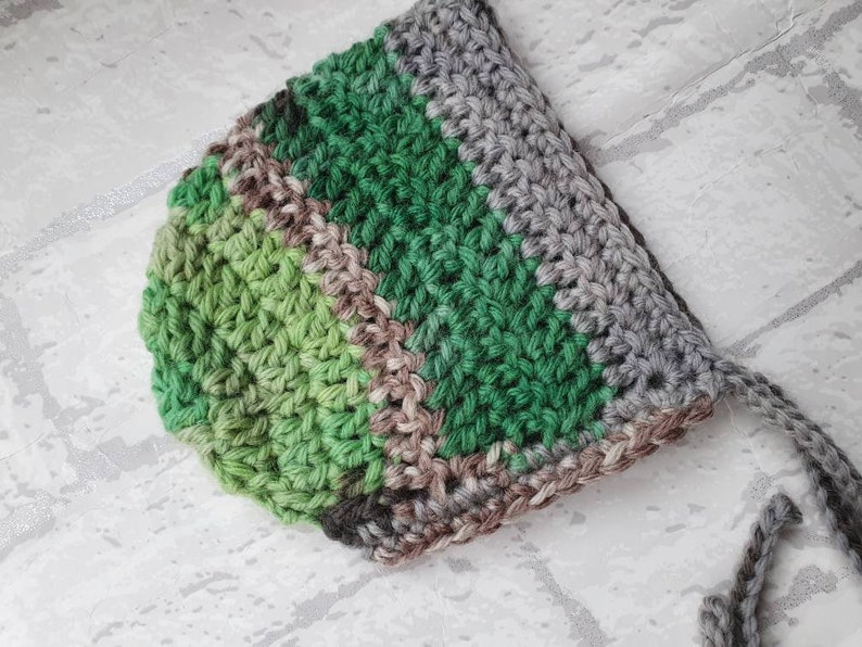 May include: A crocheted baby hat with stripes of green, brown and grey yarn.