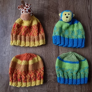 Könnte beinhalten: Vier gestrickte Mützen mit Tier-Toppern. Zwei Mützen sind gelb, orange und rot gestreift. Eine Mütze ist grün, blau und gelb gestreift. Die andere Mütze ist blau, grün und gelb gestreift. Die Topper sind eine Giraffe, ein Affe, eine Giraffe und ein Affe.