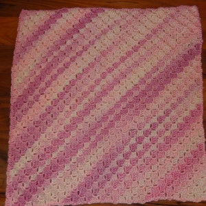 May include: A pink and white crocheted baby blanket with a diagonal pattern.