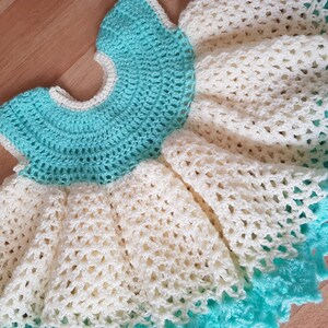 K&ouml;nnte beinhalten: Ein geh&auml;keltes Babykleid in Wei&szlig; und T&uuml;rkis. Das Kleid hat einen R&uuml;schenrock und einen runden Ausschnitt.