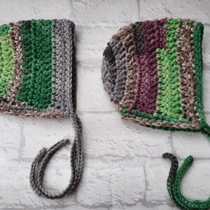 May include: Two crocheted baby bonnets with ties. One is green, brown, and grey. The other is purple, brown, and green.