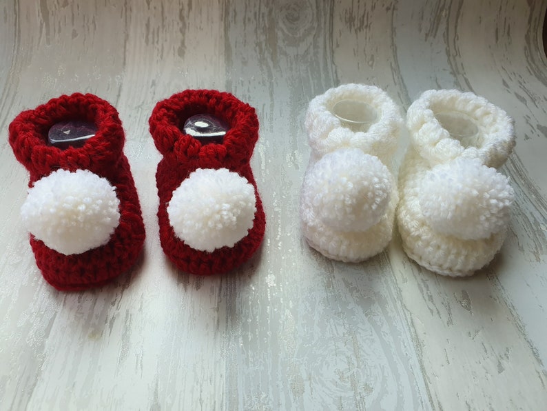 May include: Two pairs of crocheted baby booties with pom-poms. One pair is red and the other is white.