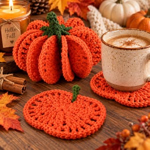 Puede incluir: Una calabaza de ganchillo naranja tridimensional con tallo verde, un posavasos plano de ganchillo con forma de calabaza naranja con tallo verde y una taza de cerámica con una bebida beige, todo con una construcción de hilo.