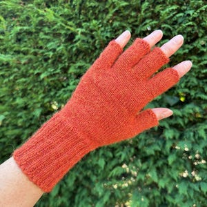 May include: A burnt orange fingerless glove featuring a ribbed knit cuff and a smooth knit hand section. The glove covers the palm and extends to the base of the fingers, leaving the fingertips exposed for dexterity and movement.