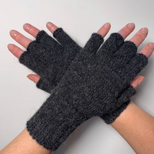 May include: A pair of dark gray fingerless gloves. The gloves are knitted with a textured pattern and have openings for the fingers and thumb. The gloves are designed to cover the hand up to the knuckles and wrist.