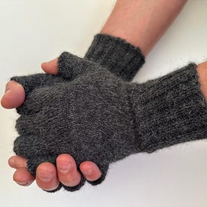 May include: A pair of dark charcoal gray fingerless gloves crafted from a fuzzy, textured knit material. The gloves feature a ribbed cuff that extends over the wrist and an open design that leaves the fingers exposed for dexterity and movement.