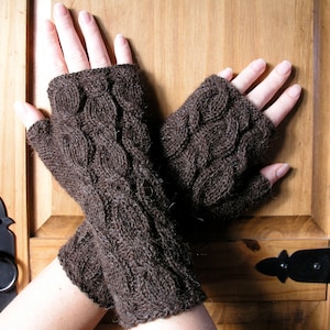 May include: A pair of dark brown fingerless gloves with a textured, cable-knit design. The gloves are made of a soft, warm material, perfect for keeping hands cozy. The gloves are shown against a wooden background.
