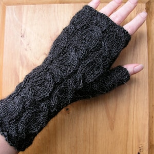 May include: Dark gray fingerless gloves with a cable knit design. The gloves are made of a soft, textured yarn and cover the hand and wrist, leaving the fingers free. The cable knit pattern adds a decorative element to the gloves.