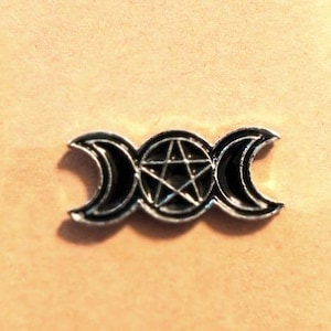 May include: A silver-toned metal pin featuring a central pentagram enclosed within a circle, flanked by two crescent moons on either side. The design includes black enamel fill within the recessed areas of the pentagram and the crescent moon shapes.