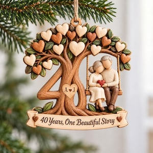 Op de afbeelding: Een hangend houten ornament in de vorm van het getal 40, met een koppel op een schommel. De boom heeft hartvormige bladeren, een hart met de letters A en J, en een banner onderaan met de tekst 40 Years, One Beautiful Story.