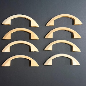 May include: Eight light-colored wooden drawer pulls arranged in two vertical columns of four. Each pull features a smooth, arched design with a curved top and flat mounting ends, showcasing a natural wood grain finish throughout the set.