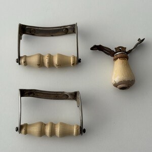 May include: Two rectangular metal drawer pulls with cream-colored, spindle-shaped wooden handles and one matching vertical handle component featuring a tapered wooden grip with visible paint wear and metallic hardware attachments.