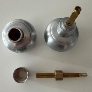 May include: Two silver-toned spherical door knobs with a smooth finish. One knob features a protruding brass-colored square spindle. Included are a small silver-toned cylindrical collar and a threaded brass-colored metal rod with a central nut.