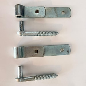 May include: Two sets of silver-colored metal gate hinges, each consisting of a flat strap hinge with two square mounting holes and a corresponding screw-in pintle pin with a threaded shank for secure installation into wood or masonry surfaces.
