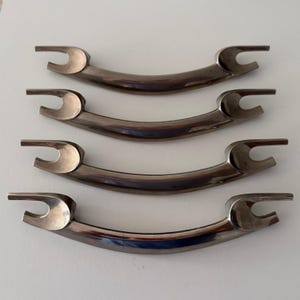 May include: A set of four matching silver-toned metal drawer pulls. Each handle features a smooth, curved central bar with distinct, open-ended fork-like mounting brackets on both ends, providing a sleek and functional design for cabinetry.