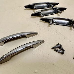 May include: A set of five silver-toned metal drawer pulls with a smooth, curved design. Three of the pulls are positioned with their mounting screws attached, while two are separate. Four small, individual metal mounting screws are also included.