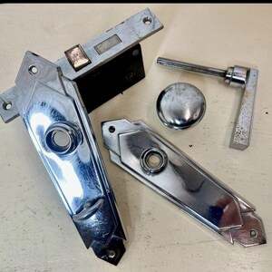 May include: A set of chrome-plated door hardware including a rectangular mortise lock mechanism, two elongated diamond-shaped escutcheon plates with central circular openings, a round door knob, and a single L-shaped lever handle with a threaded spindle.