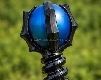 May include: A staff topper featuring a central metallic blue sphere encased in a black, multi-pointed frame. The base consists of a black, spiraled, screw-like structure. The text CARVINGMASTERS is visible across the center of the blue sphere.