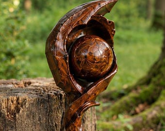 May include: A hand-carved wooden staff featuring a polished, spherical brown gemstone orb cradled within a textured, organic-shaped wooden setting. The wood displays a deep, glossy finish with intricate, carved details surrounding the central sphere.
