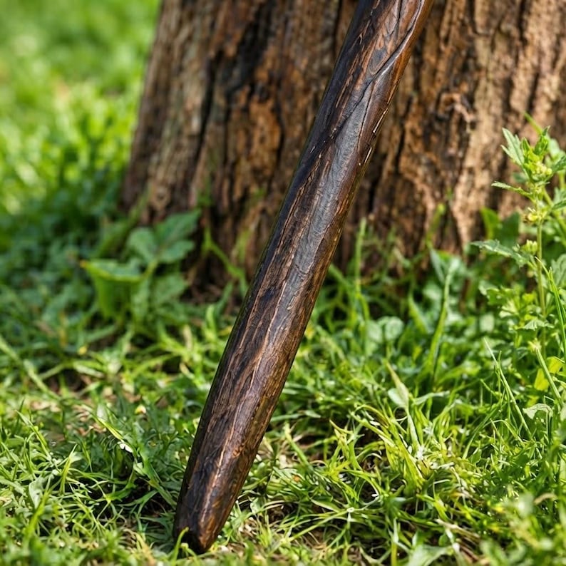 Puede incluir: Un bast&oacute;n de madera largo y cil&iacute;ndrico con un acabado pulido en color marr&oacute;n oscuro. La superficie del bast&oacute;n presenta un patr&oacute;n de veta tallada y texturizada que recorre verticalmente su longitud, mostrando variaciones naturales y brillo.