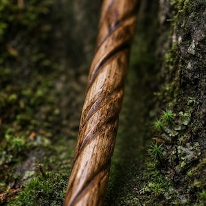 Może przedstawiać: Cylindryczny drewniany kostur z ciągłym, głębokim spiralnym rzeźbieniem biegnącym wzdłuż całej długości. Drewno ma naturalne brązowe usłojenie z ciemniejszymi odcieniami w zagłębieniach wzoru spiralnego oraz gładkie, wypolerowane wykończenie.