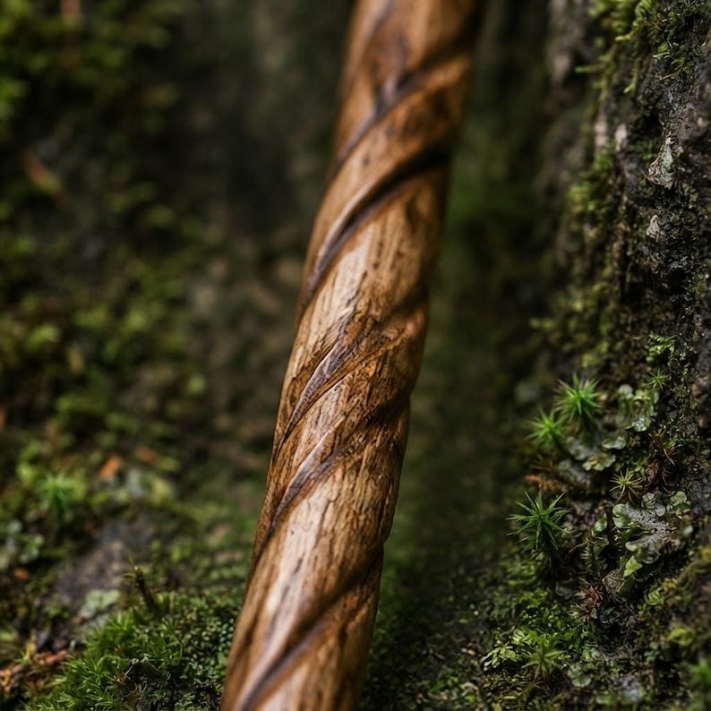 Może przedstawiać: Cylindryczny drewniany kostur z ciągłym, głębokim spiralnym rzeźbieniem biegnącym wzdłuż całej długości. Drewno ma naturalne brązowe usłojenie z ciemniejszymi odcieniami w zagłębieniach wzoru spiralnego oraz gładkie, wypolerowane wykończenie.