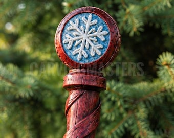 May include: A wooden staff featuring a dark reddish-brown finish with a spiral carved texture. The top is adorned with a circular emblem containing a raised white snowflake design set against a textured light blue background.
