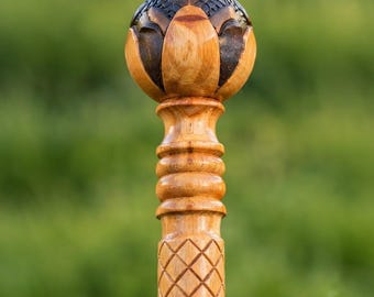 May include: A wooden walking stick featuring a spherical top carved into a lotus-like shape with dark brown and light tan wood tones. The shaft below the sphere has a series of horizontal rings and a diamond-patterned texture carved into the wood.