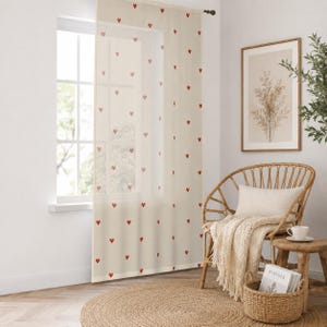 May include: A sheer, off-white curtain panel featuring a repeating pattern of small, solid red hearts. The lightweight fabric hangs from a dark rod, allowing soft light to filter through while displaying the scattered heart motif across the surface.