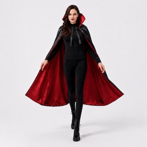 May include: A full-length hooded cape featuring a black exterior and a vibrant red interior lining. The garment includes a high, structured collar and black ribbon ties at the neck, designed to drape over the shoulders and down to the floor.