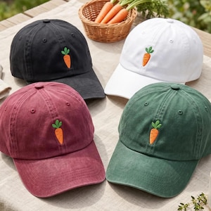Op de afbeelding: Vier baseballpetten in zwart, wit, bordeauxrood en donkergroen, elk voorzien van een geborduurde oranje wortel met groene blaadjes op het voorpaneel. De petten hebben een gestructureerde kroon, een gebogen klep en ventilatiegaatjes.