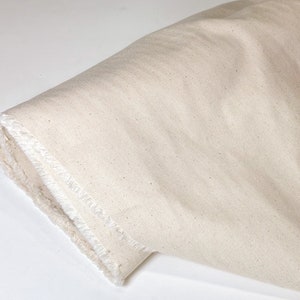 May include: A close-up of a natural-colored fabric with a slightly rough texture. The fabric is folded and has a raw edge.