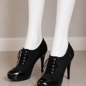 May include: A pair of black lace-up high heel shoes featuring a matte fabric upper, a glossy patent leather toe cap, and a matching patent leather heel counter. The shoes include a platform sole, thin black laces, and silver-toned eyelets.