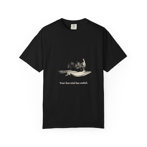 Pode incluir: Uma t-shirt preta de manga curta com um gráfico central de uma pessoa com a cabeça entre as mãos sobre um livro. Abaixo da ilustração, o texto branco diz: Your free trial has ended. A t-shirt tem um decote redondo.