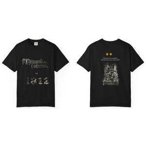 May include: A black short-sleeve t-shirt featuring a front graphic with the text Hansel u. Gretel est. 1812. The back displays two orange stars, the text The food was exquisite, but the host was a real witch!, and a detailed black and white illustration.