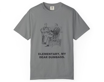 May include: A grey short-sleeve t-shirt featuring a black and white vintage-style illustration of two men sitting in chairs. Below the illustration, the text reads: ELEMENTARY, MY DEAR DUMBASS. The shirt has a crew neckline and a standard fit.