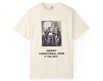 May include: A cream-colored short-sleeve t-shirt featuring a black and white vintage-style illustration of two figures in a room. Below the graphic, the text reads: MERRY CHRISTMAS. NOW F*CK OFF. The shirt has a crew neckline and a standard fit.