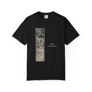 Puede incluir: Una camiseta negra de manga corta con un gráfico rectangular vertical en el lado izquierdo. El gráfico muestra una ilustración en blanco y negro de un gato asomándose. A la derecha del gráfico, el texto dice, Is this a bad time?