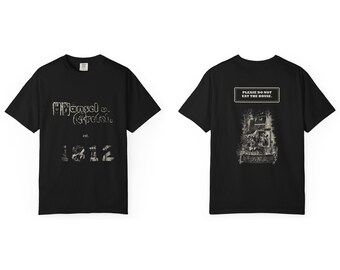 May include: A black short-sleeve t-shirt featuring a front graphic with the text Hansel v. Gretel est. 1812. The back of the shirt displays a detailed illustration of a house with the text PLEASE DO NOT EAT THE HOUSE.