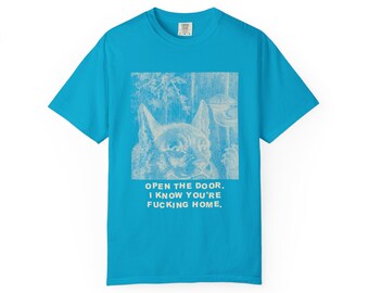 May include: A bright blue short-sleeve t-shirt featuring a white graphic print of a cat and the text: OPEN THE DOOR. I KNOW YOU'RE FUCKING HOME. The shirt has a crew neckline and a standard fit, with a visible brand label at the inner collar.