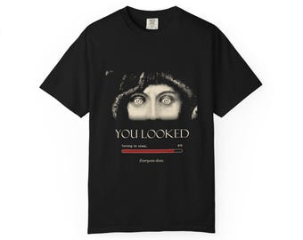 Puede incluir: Una camiseta negra de manga corta con un gráfico de ojos humanos sobre el texto YOU LOOKED. Debajo, una barra de carga indica Turning to stone... 87%, seguida del texto Everyone does. La camiseta tiene un cuello redondo clásico.