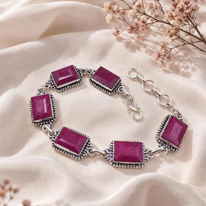 Peut inclure: Un bracelet à maillons en argent orné de cinq pierres rectangulaires de couleur magenta profond. Chaque pierre est sertie dans un cadre en argent oxydé texturé avec une bordure perlée. Le bracelet comprend une chaînette d'extension.
