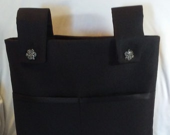 May include: A black fabric tote bag with two pockets on the front and two decorative embellishments on the top.