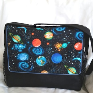 May include: A black messenger bag with a space-themed fabric design. The fabric features planets, stars, and swirling galaxies in shades of blue, orange, red, and green.